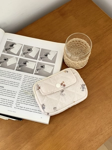 Close-up of beige quilted floral coin purse placed on an open book in natural light