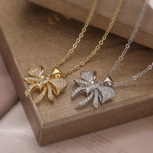 Gold and silver bow pendant necklaces with zircon crystals on a brown jewelry display box