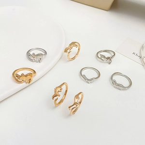 Detail of artistic dinosaur-themed open rings in gold and silver finishes on white tray