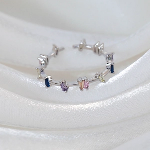 Macro shot of silver ring with multi-colored rectangular zircon stones on white fabric