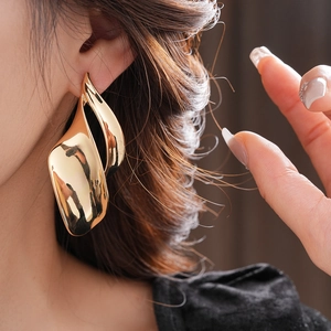 Detailed view of large twisted leaf-shaped gold stud earrings on model for a modern look