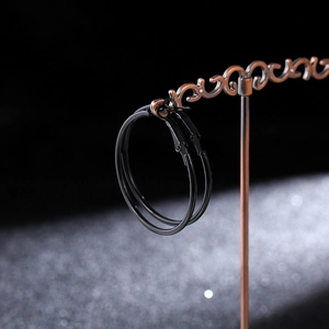 Close-up of black hoop earrings on vintage bronze display stand with a dark starry backdrop