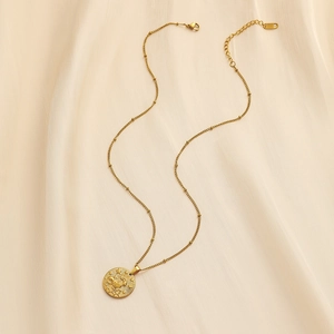 Macro detail of golden stainless steel necklace with round zodiac pendant on silk
