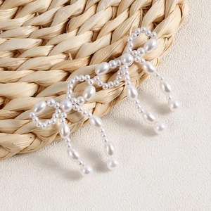 Detail of handmade pearl bow earring with drop pearls on a woven straw mat texture
