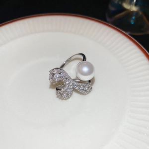 Detail of silver bow ring with white pearls and zircons on a white ceramic plate