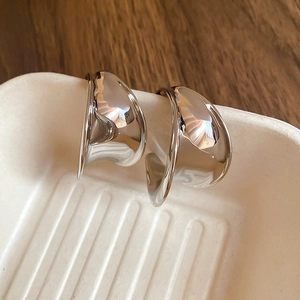Macro detail of silver C-shaped chunky hoop earrings with a liquid metal mirror finish