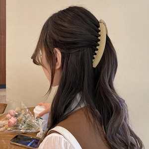 Matte beige banana clip hair accessory shown on a model in a cozy cafe setting