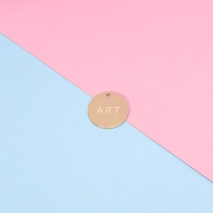 Close-up of golden stainless steel round pendant with ART engraving on bicolor background