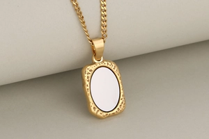 Close-up of golden rectangular pendant with hammered frame and smooth white inlay detail