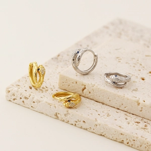 Macro shot of silver and gold snake earrings with zircon stones on stone display