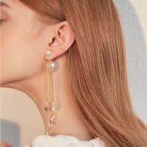 Detailed view of long gold tassel earrings with imitation pearls on a side profile model