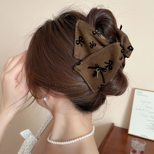 Detail of herringbone fabric bow hair clip with black pattern and gold charm accessory