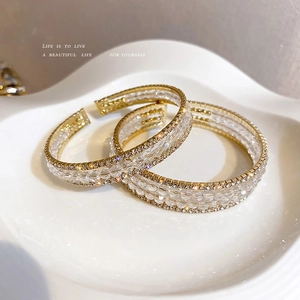 Exaggerated double-layered open cuff bracelet with white crystals on a gold base