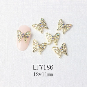 Detail of 12x11mm golden butterfly nail art charms with colorful rhinestones on a pink nail