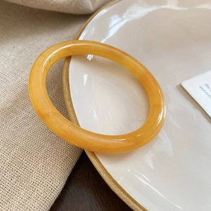 Close-up of amber resin round bangle on minimalist ceramic tray with fabric background