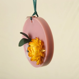 Pink round scented wax tablet with yellow dried flowers and a green ribbon hanging strap