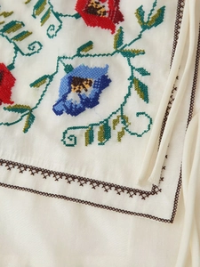 Détail de la broderie florale au point de croix et bordure sur un gilet ethnique blanc