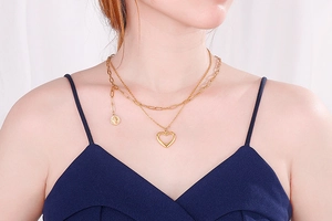 Detail showing a layered gold necklace with a round coin and hollow heart pendant