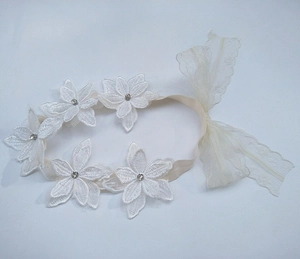 Dettaglio fascia neonata bianca con fiore in pizzo, strass e morbido elastico
