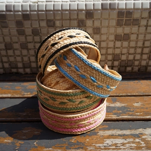Detail of four colorful woven straw headbands with contrast trim on a rustic wood surface