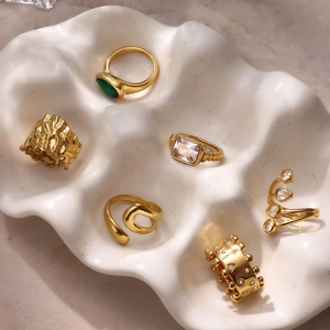 Collection de bagues dorées en acier inoxydable avec zircon et émeraude sur plateau blanc