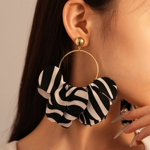 Detail von Ohrringen mit Zebra-Stoffmuster und goldenen geometrischen Ringen am Model