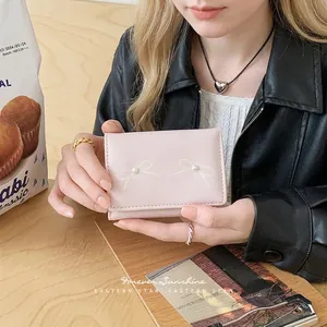 Pink trifold wallet with bow prints and pearl detail held by model in casual setting