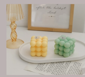 Close-up of cube bubble scented candles in cream yellow and mint green on white tray