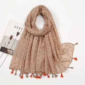 Flat lay of beige floral cotton scarf with tassel fringe details on a white background