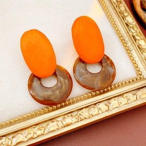 Detail of geometric resin and wood earrings featuring orange oval and brown marble ring