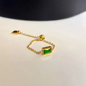 Detailed macro view of adjustable gold chain ring with emerald green zircon and heart charm