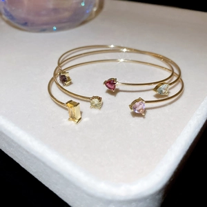 Detailed view of two gold-plated open bangles with colorful heart and square zircon gems