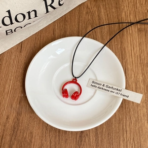 Détail du collier pendentif casque rouge posé dans une coupelle en céramique blanche
