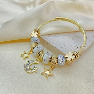 Chic gold wire bangle with star and moon charms on elegant satin and stone background
