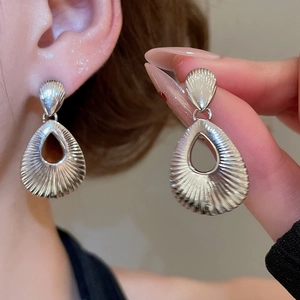Close-up of silver teardrop earrings with radial texture shown on model and held by hand