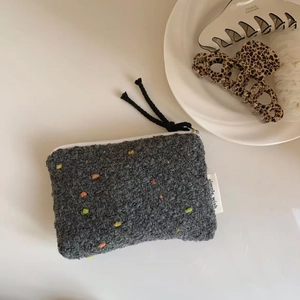 Dettaglio del portamonete in tweed grigio con puntini colorati ed etichetta laterale
