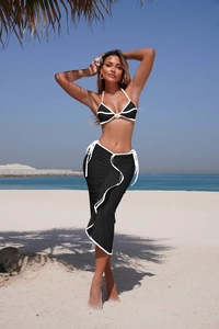 Detail of a black bikini set with white piping and a matching long beach skirt outdoors