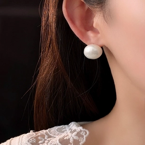 Close-up of a large white round pearl earring worn on model against a dark background