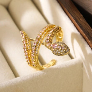 Macro shot of gold snake ring with pink and clear zircons on beige velvet cushion