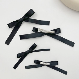 Set of four black satin bow hair clips with silver metal duckbill clips on white background