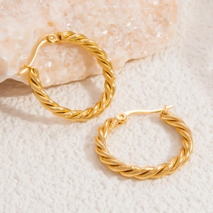 Close-up of gold 18k plated twisted hoop earrings on a minimalist stone background