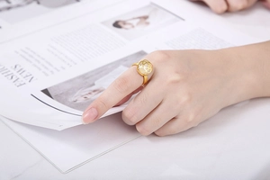 Detail of a gold floral镂空 design ring worn on a finger over a fashion magazine background