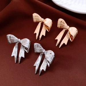 Detail of stylish gold and silver bow stud earrings on a textured deep red fabric surface