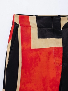Detail of high-waist geometric print pants with red and black stitching accents