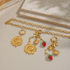 Floral gold jewelry set with sunflower and strawberry pendants on a beige background
