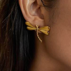 Vue macro d'une boucle d'oreille libellule dorée avec ailes givrées portée sur l'oreille