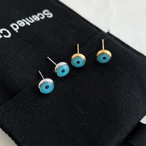 Macro detail of silver and gold Evil Eye stud earrings featuring blue enamel and metal finish