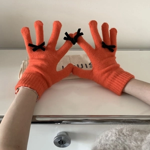 Close-up of orange knitted gloves featuring black bow accents and touchscreen finger tips