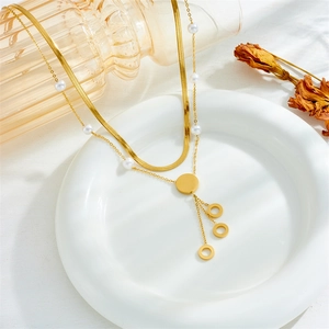 Detailed close-up of a double-layered gold snake chain necklace with pearls on a white plate