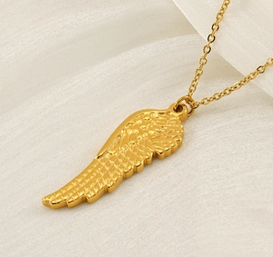 Detailed view of gold angel wing pendant on a white silk background texture
